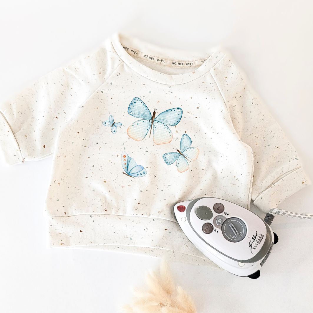 Anwendungsbeispiel: Baby-Sweatshirt mit aufgebügeltem Schmetterlingsmotiv in Blau und Apricot – langlebiger, flexibler Druck für handmade Kleidung.