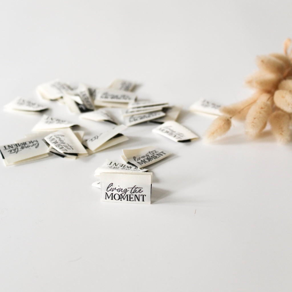 Detailaufnahme des Webetiketts "Living the Moment" für DIY-Nähprojekte – stilvoll und hochwertig verarbeitet